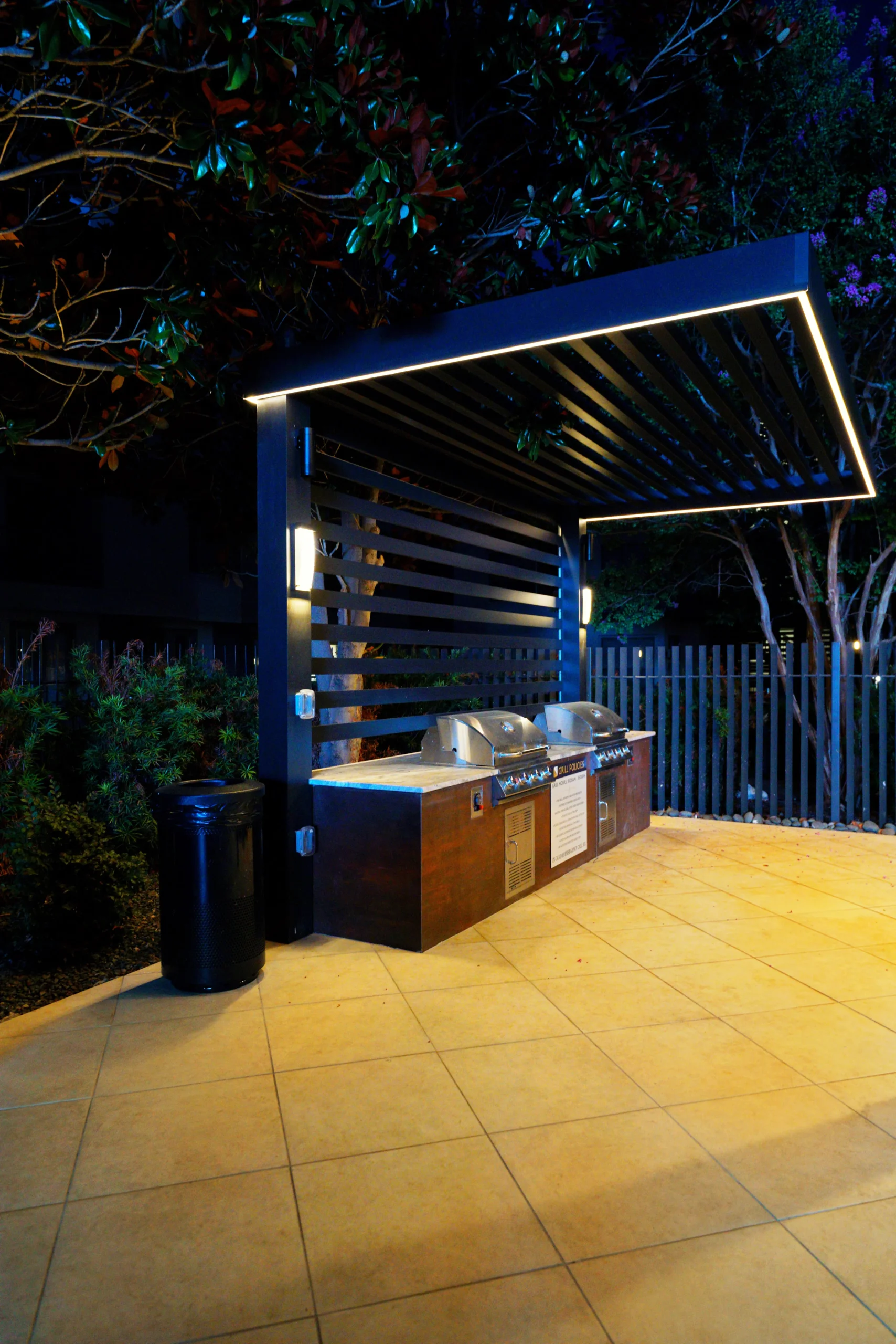LED-lit slatted cantilever over an outdoor kitchen at night