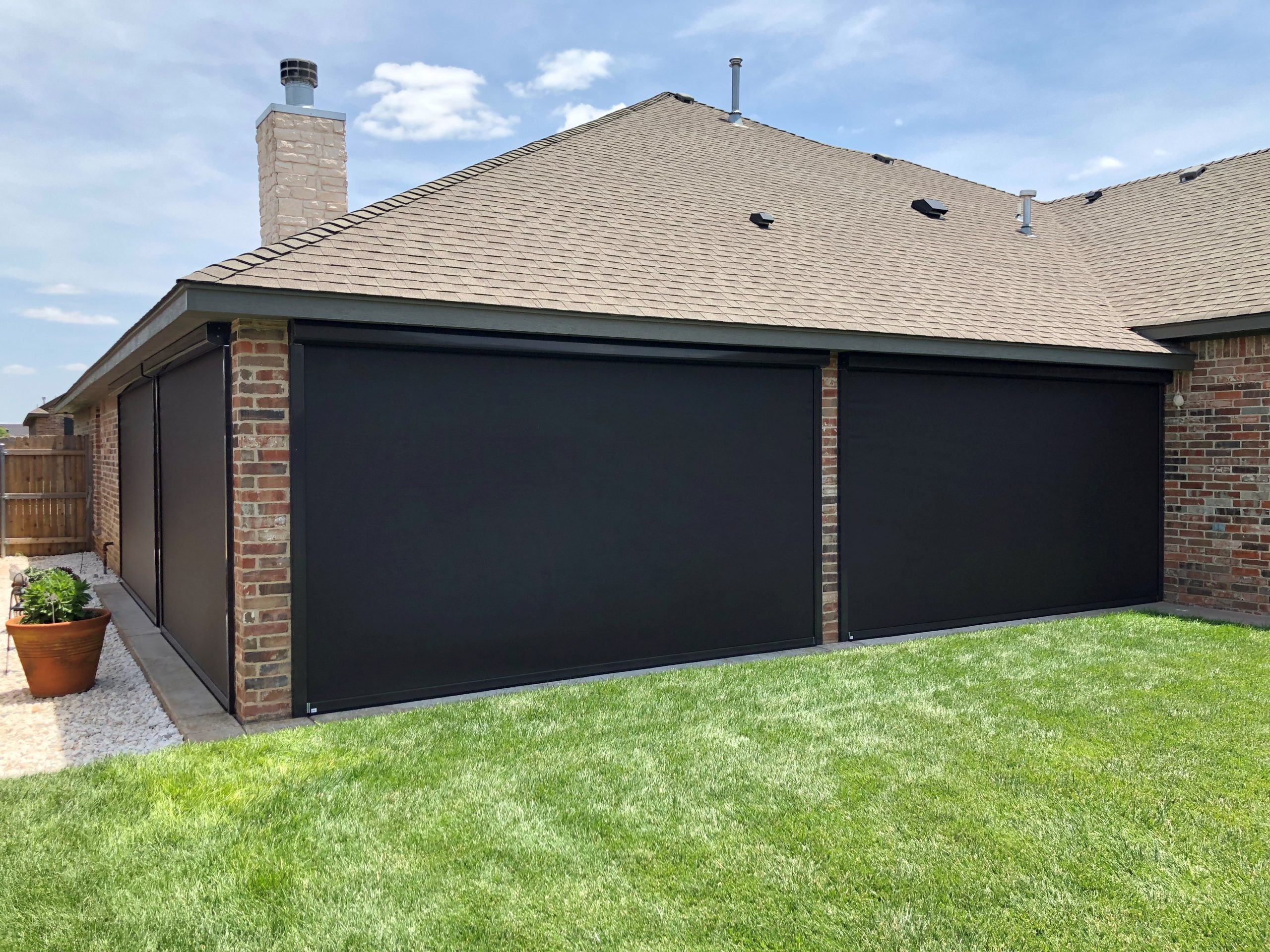 Brick home corner with three tall black retractable screens down on an L-shaped patio