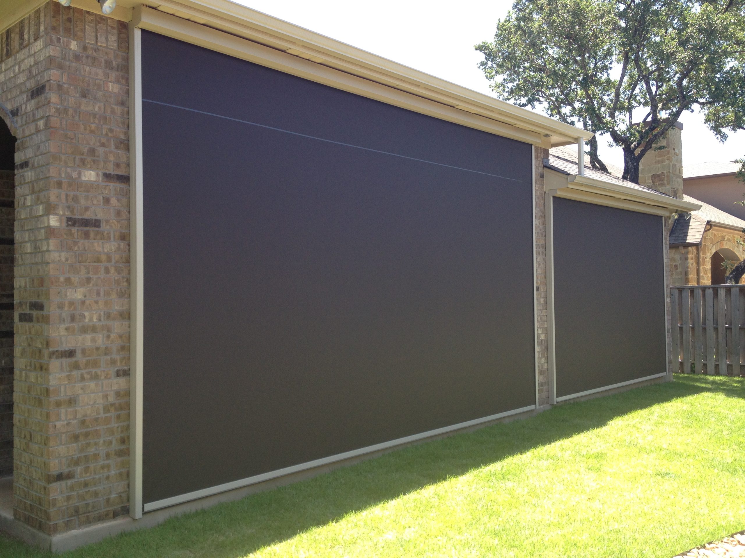 Brick wall with two bronze motorized retractable screens beside a mature oak