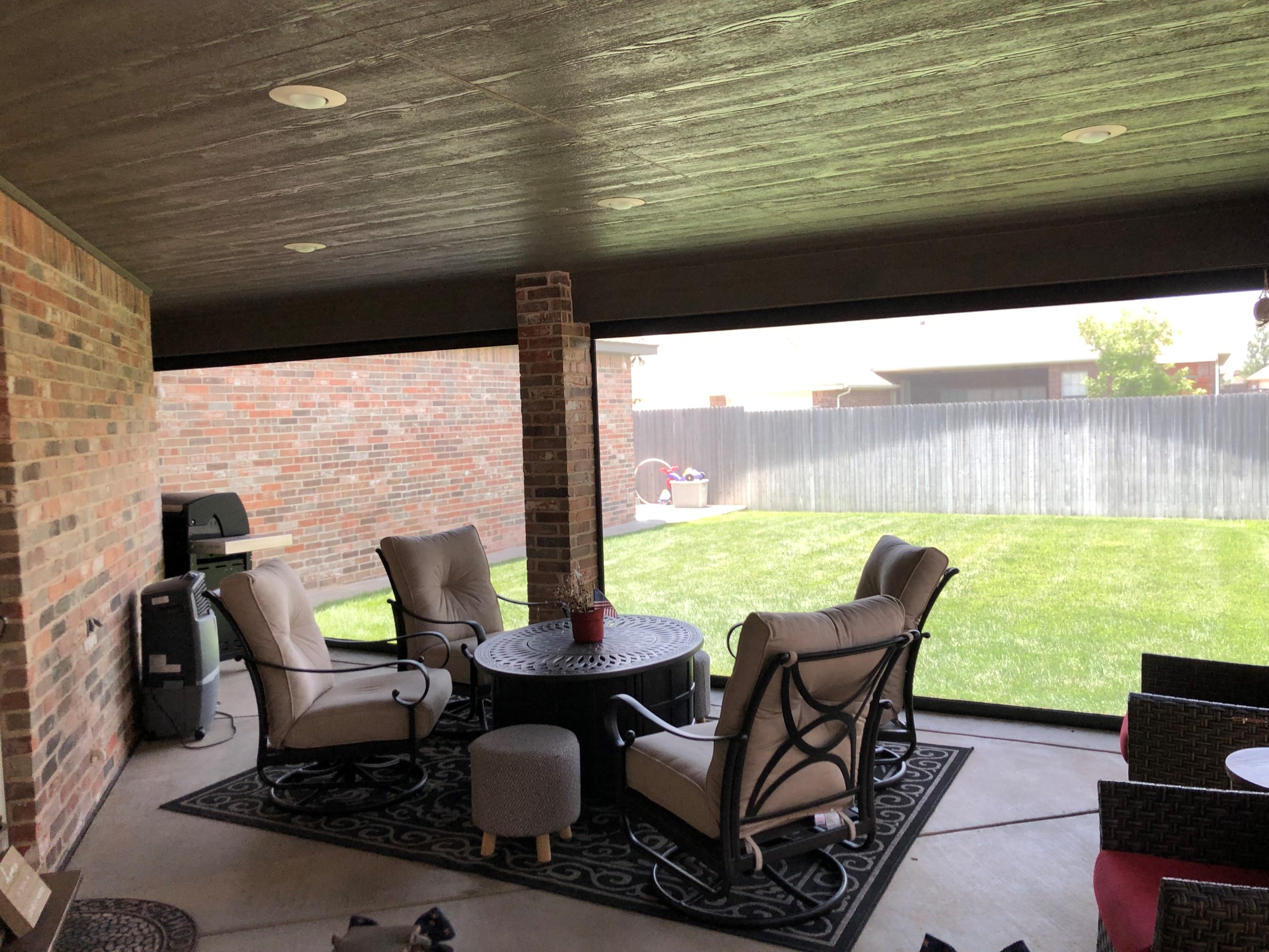 Covered patio with wood ceiling, recessed lighting, and screen partially lowered between brick columns