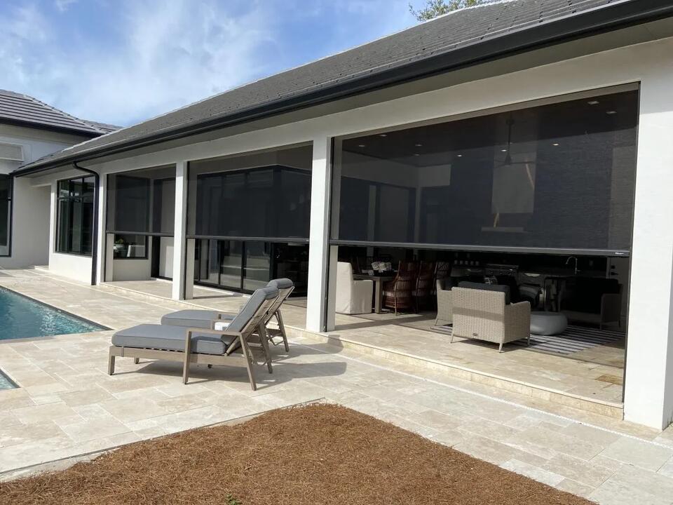 Luxury pool patio with four dark retractable screens lowered between white columns, travertine deck