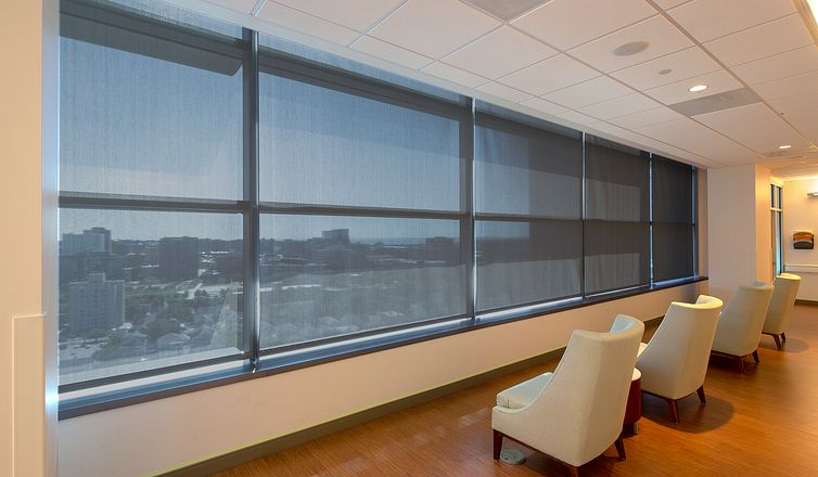 Top-floor commercial waiting area with a row of interior roller shades overlooking a city skyline