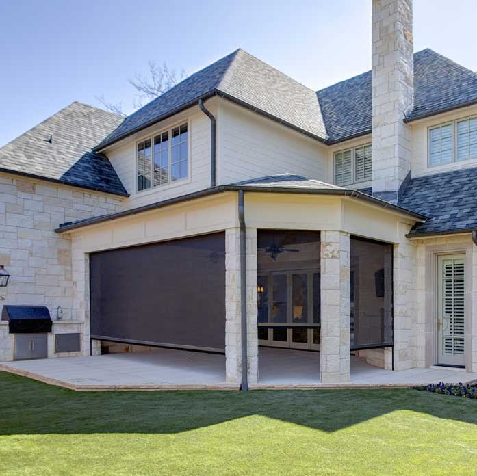 Stone and siding home with a bronze retractable screen lowered on a covered outdoor kitchen