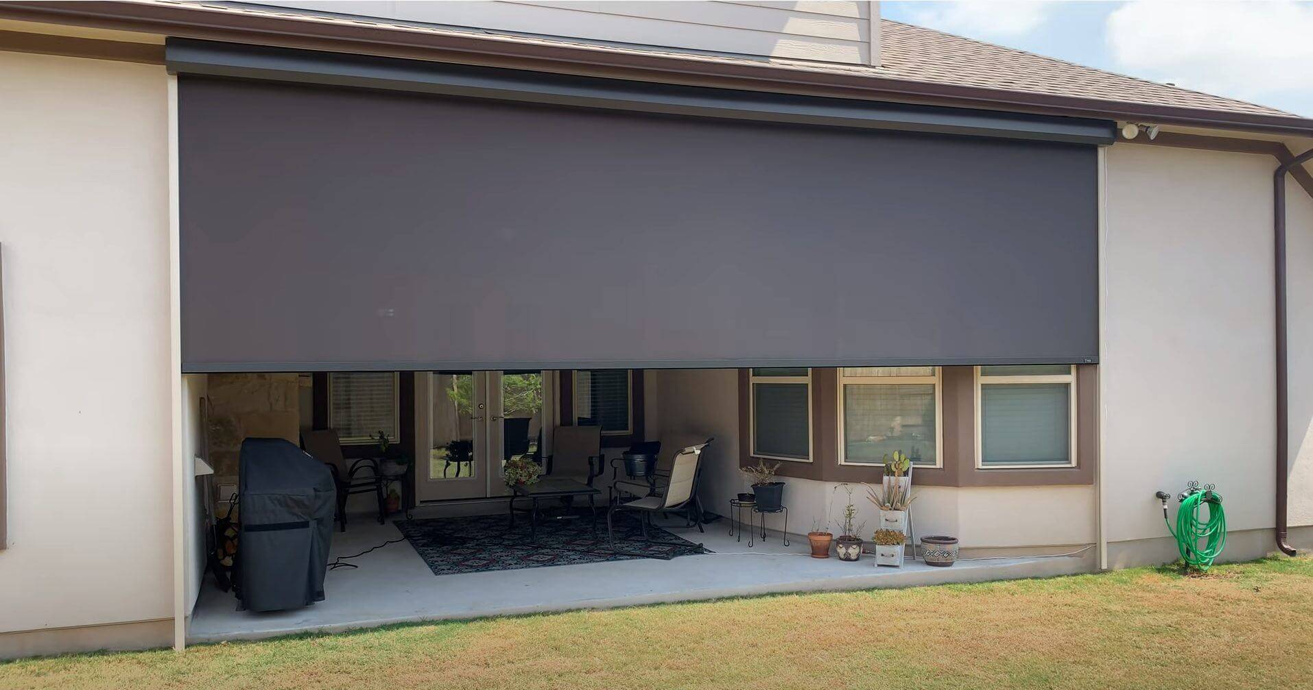 Rear of a stucco home with a wide gray retractable screen partially lowered over a patio