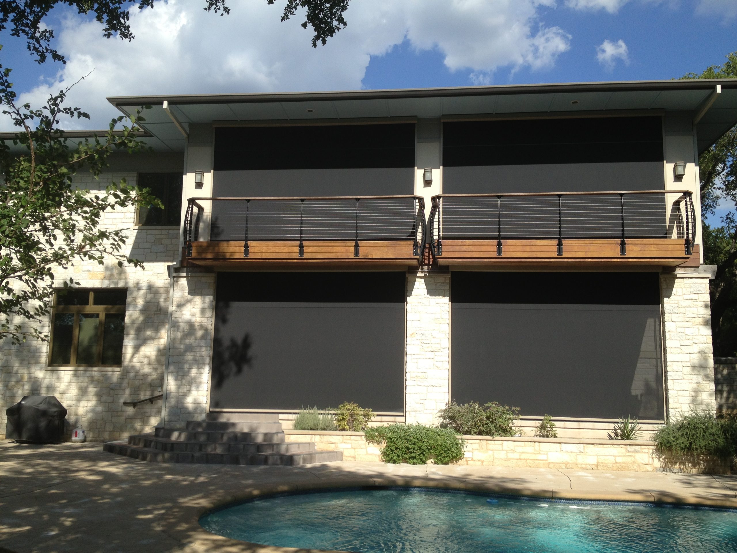 Two-story modern stone home with four retractable screens across both levels above a pool