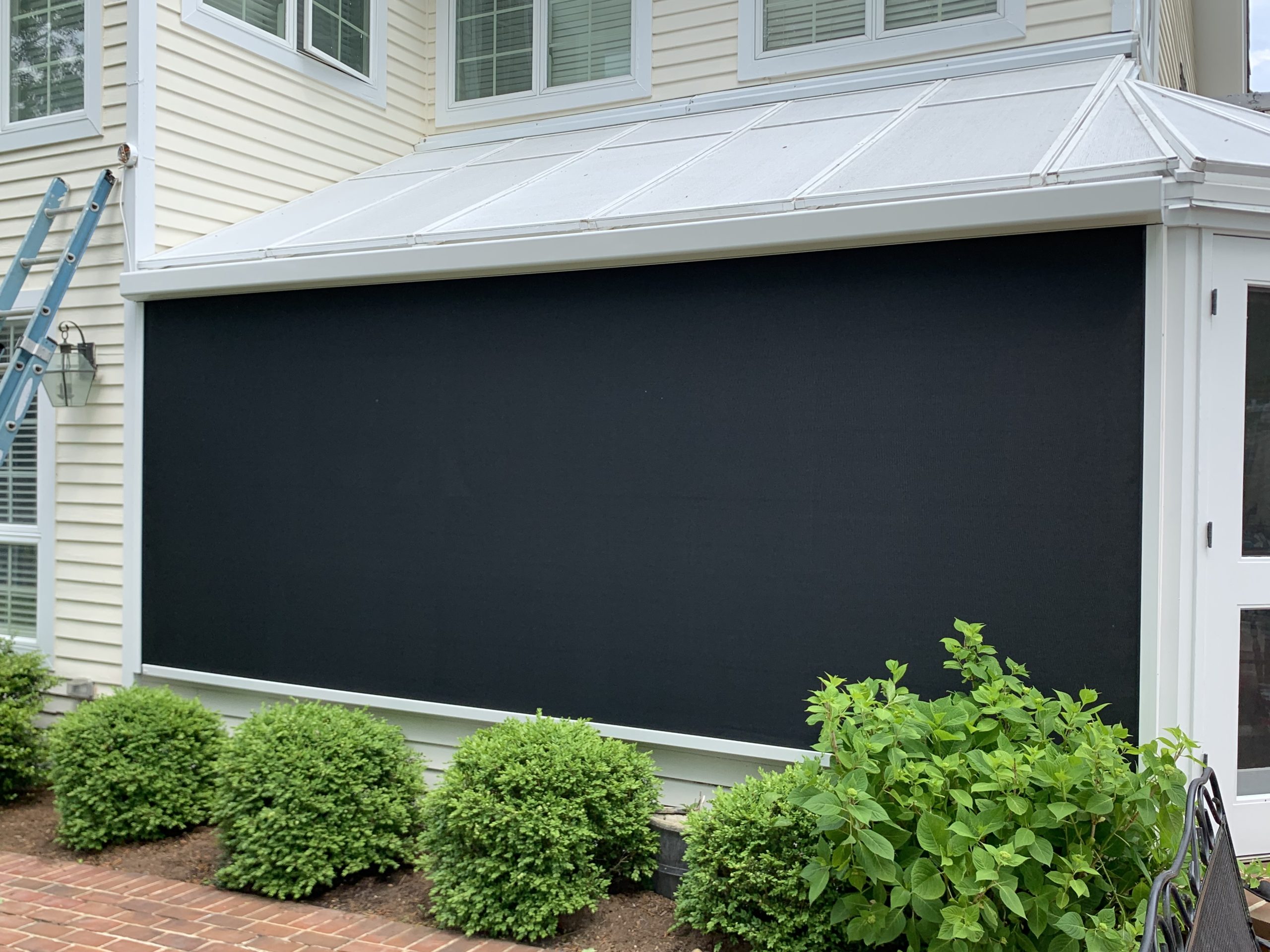 White clad sunroom enclosure with a black motorized screen lowered over the opening